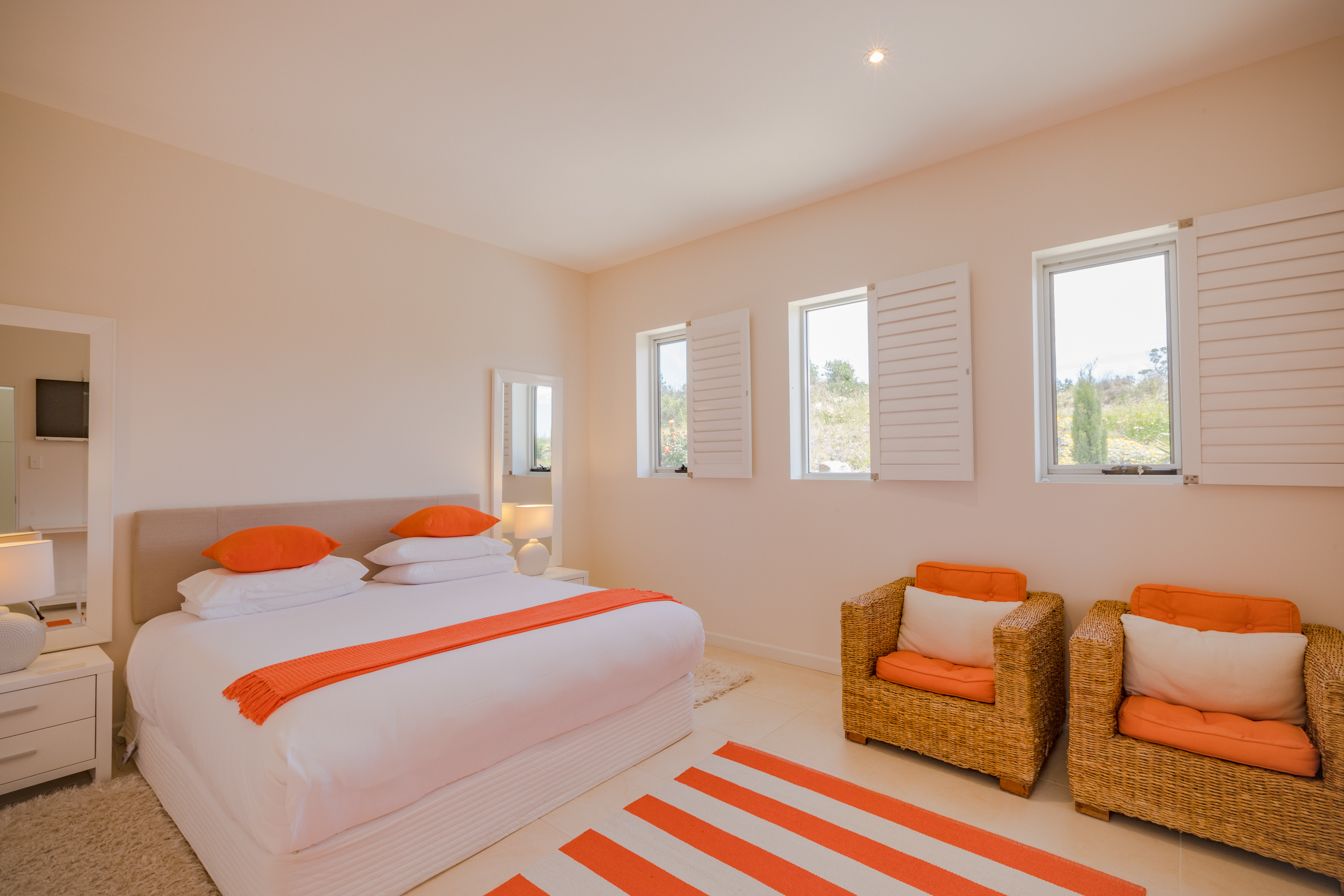 A bedroom with a large bed, two wicker chairs, and a window with shutters.