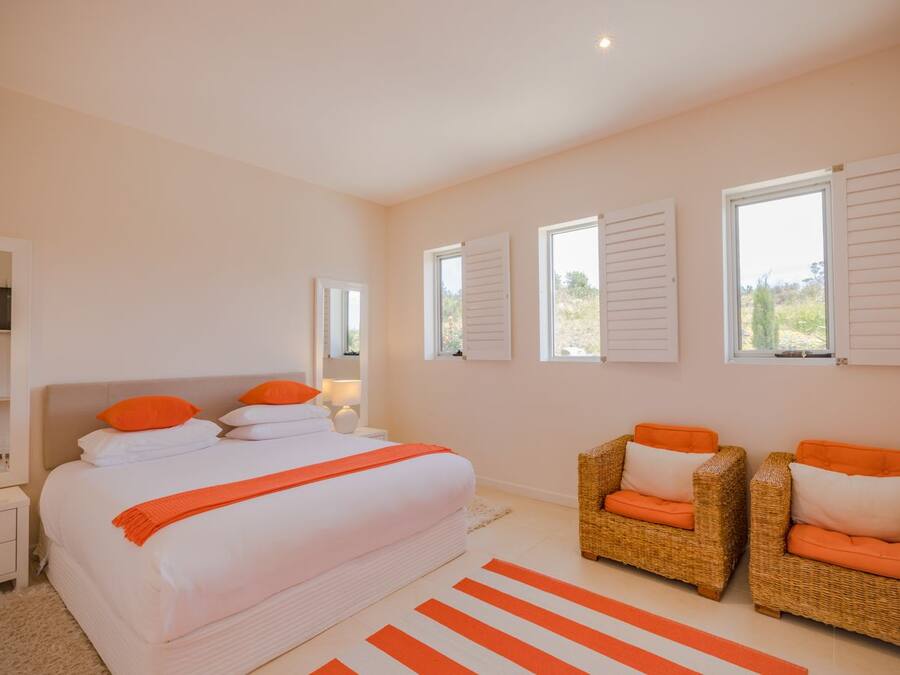 A bedroom with a large bed, two wicker chairs, and a window with shutters.