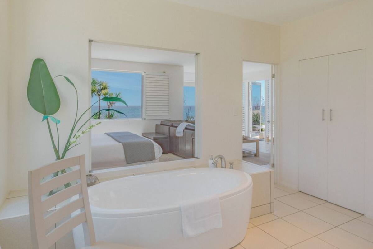 A modern bathroom with a large bathtub, a shower area, and a view of the ocean through a window.
