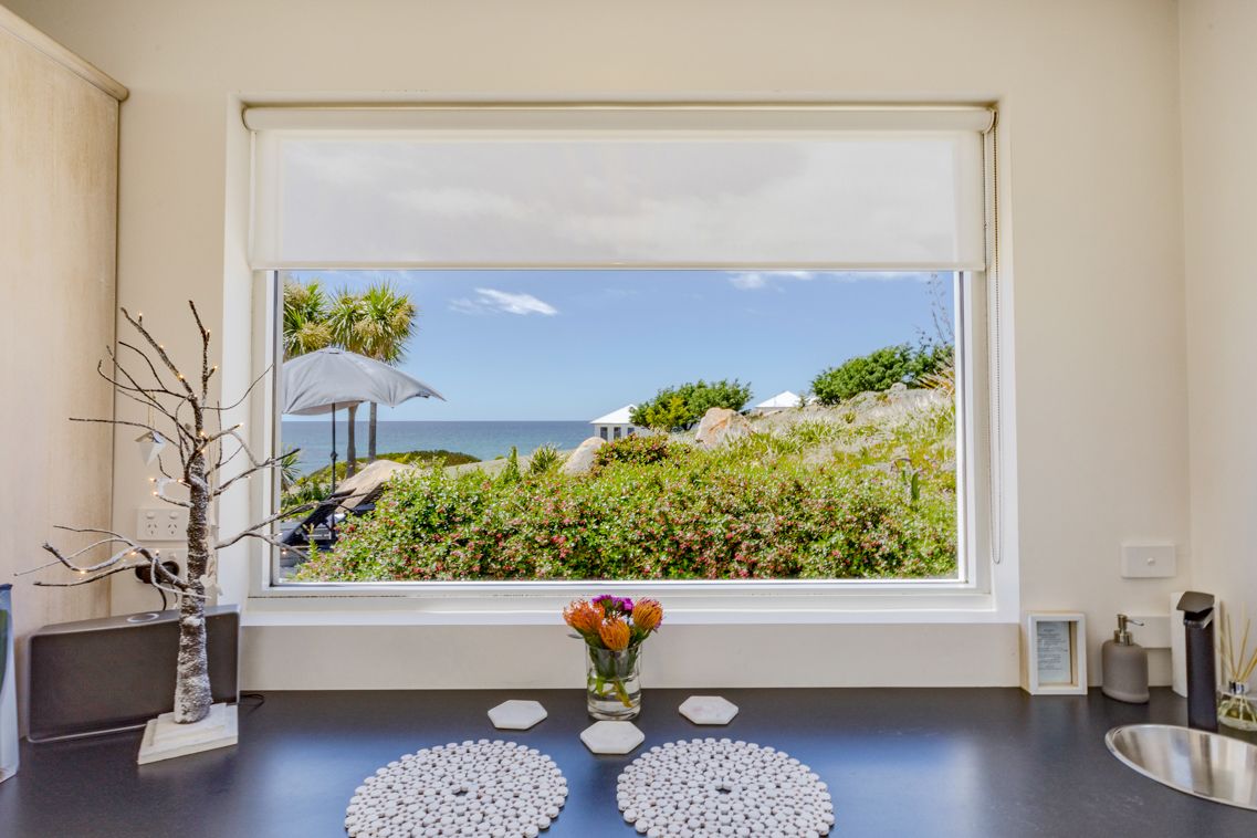 A room with a large window overlooking a beach, a small table with decorative items, and a view of the ocean and greenery.