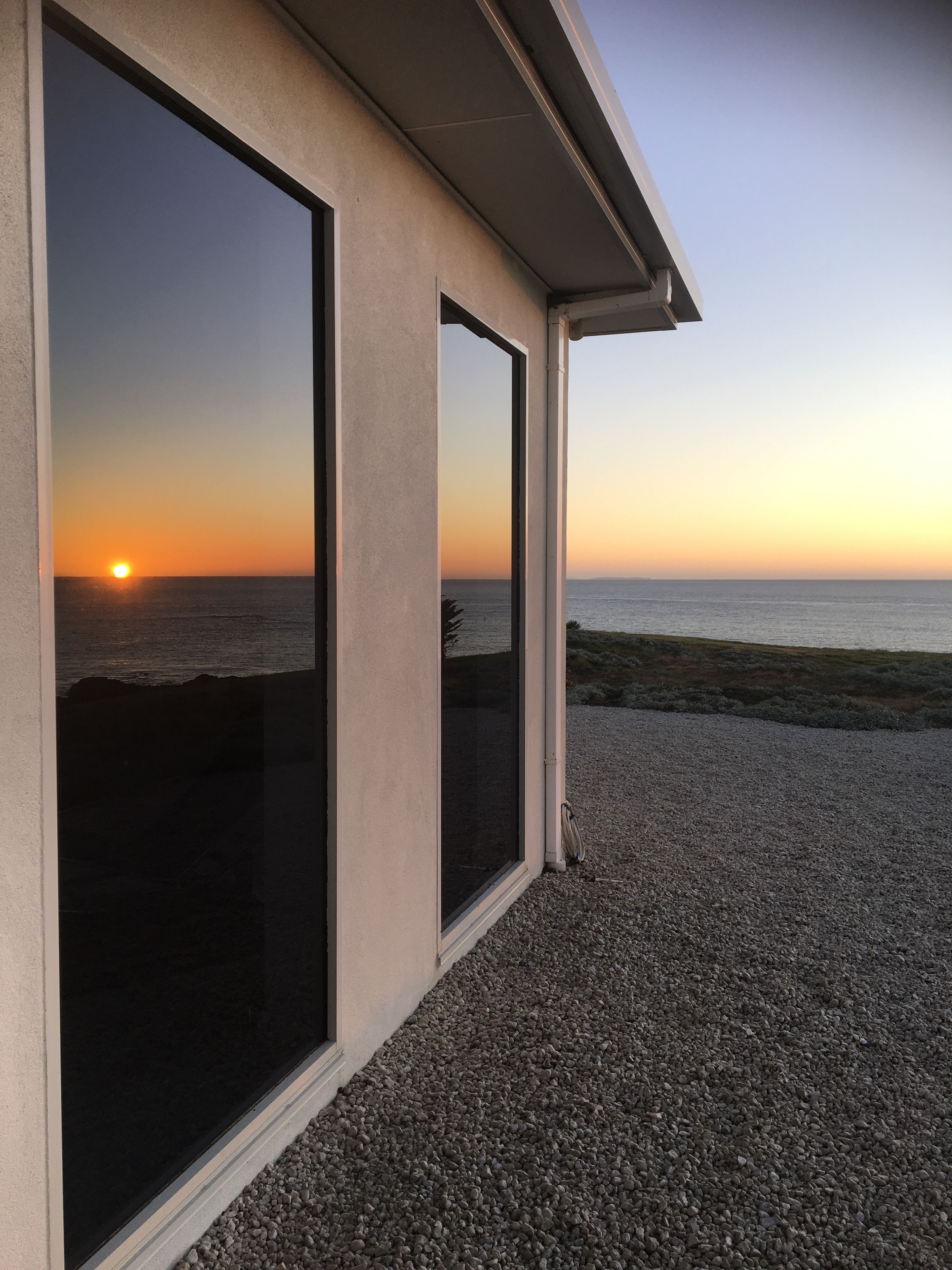 Un edificio con grandes ventanales que dan a una playa al atardecer.