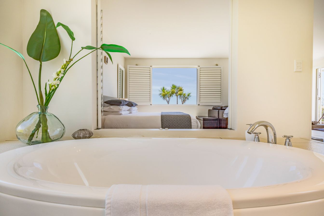 Un baño moderno con una bañera grande, un espejo y una ventana que ofrece vistas a palmeras.