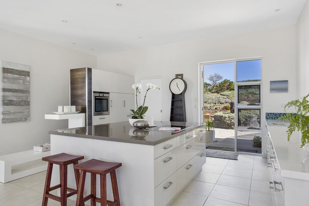 A modern kitchen with a large island, bar stools, and a view of the outdoors.