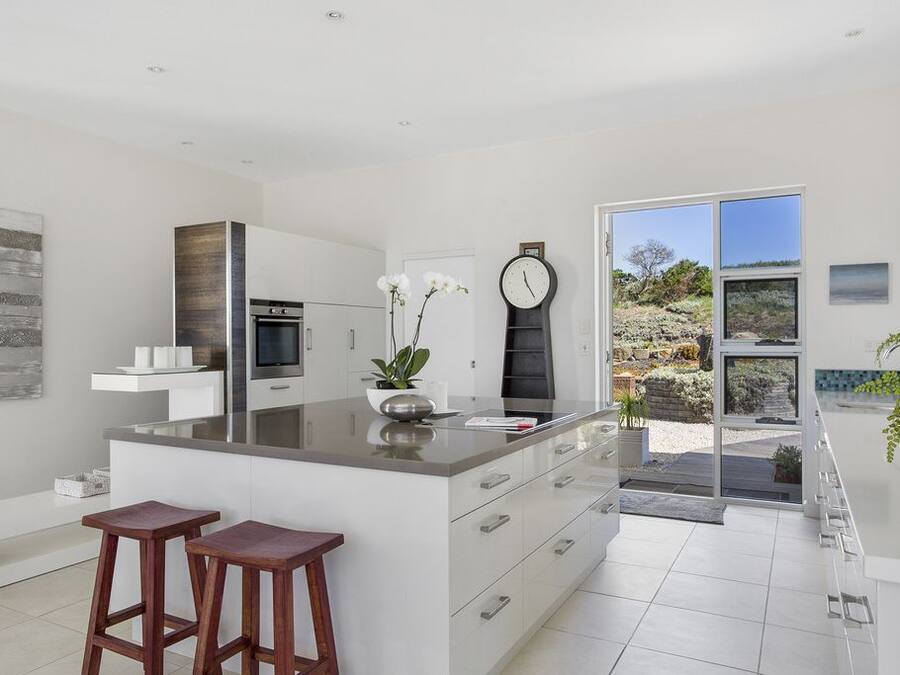 A modern kitchen with a large island, bar stools, and a view of the outdoors.
