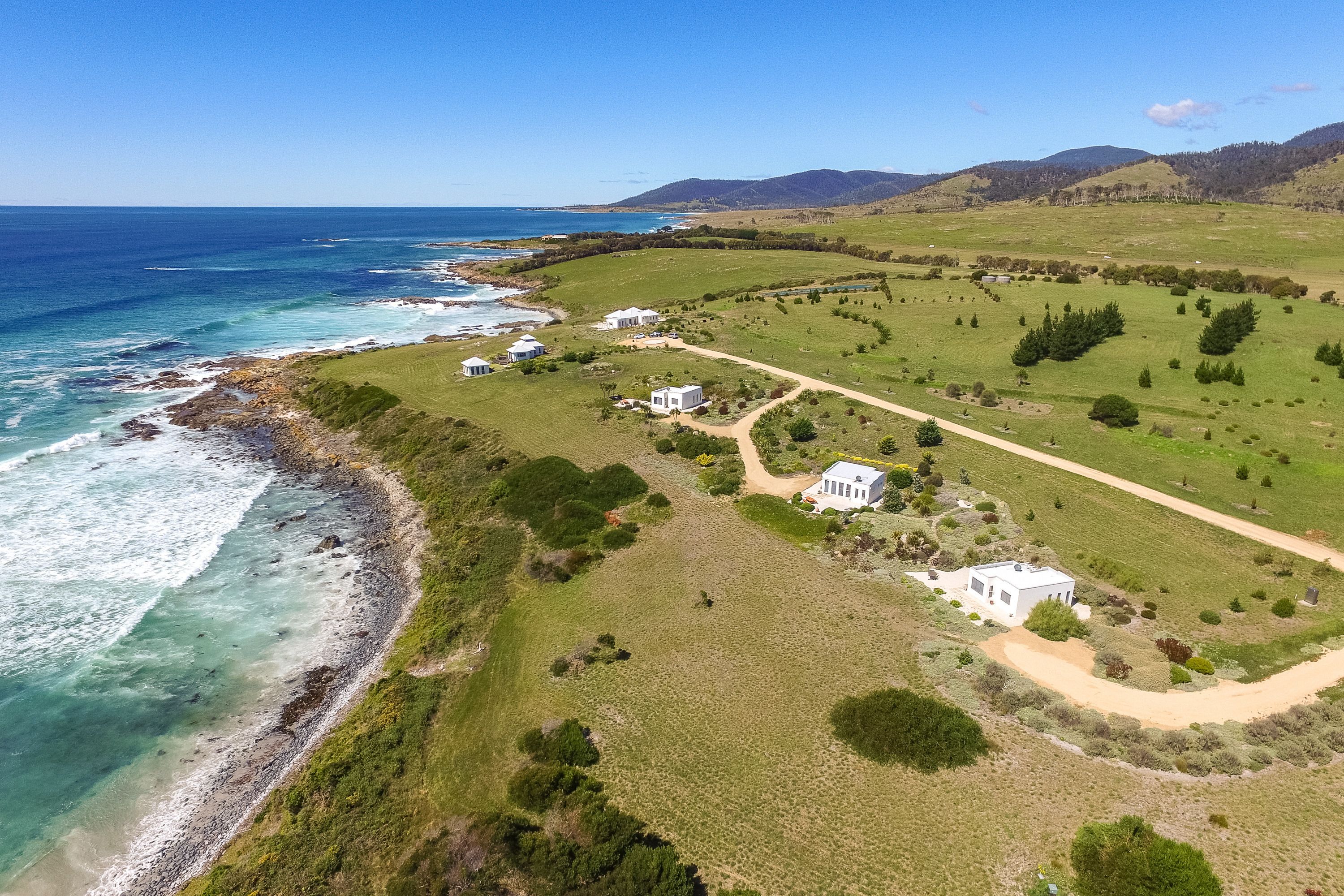 An aerial view of a coastal property with multiple houses, a dirt path, and a beach.