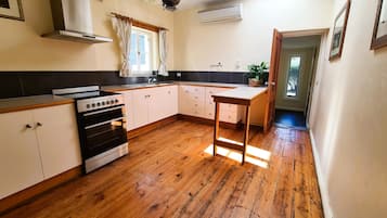 A kitchen with wooden flooring, a stove, cabinets, a sink, and a window with curtains.