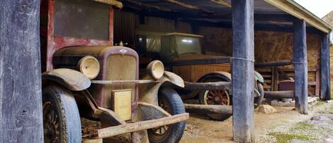 An old, rustic building with a wooden structure and a vintage car parked inside.