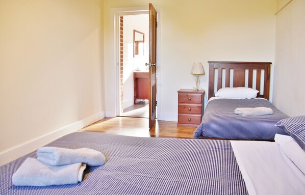 A bedroom with two beds, a wooden dresser, and a bathroom visible through an open door. - Bungaree Station (Bungaree)