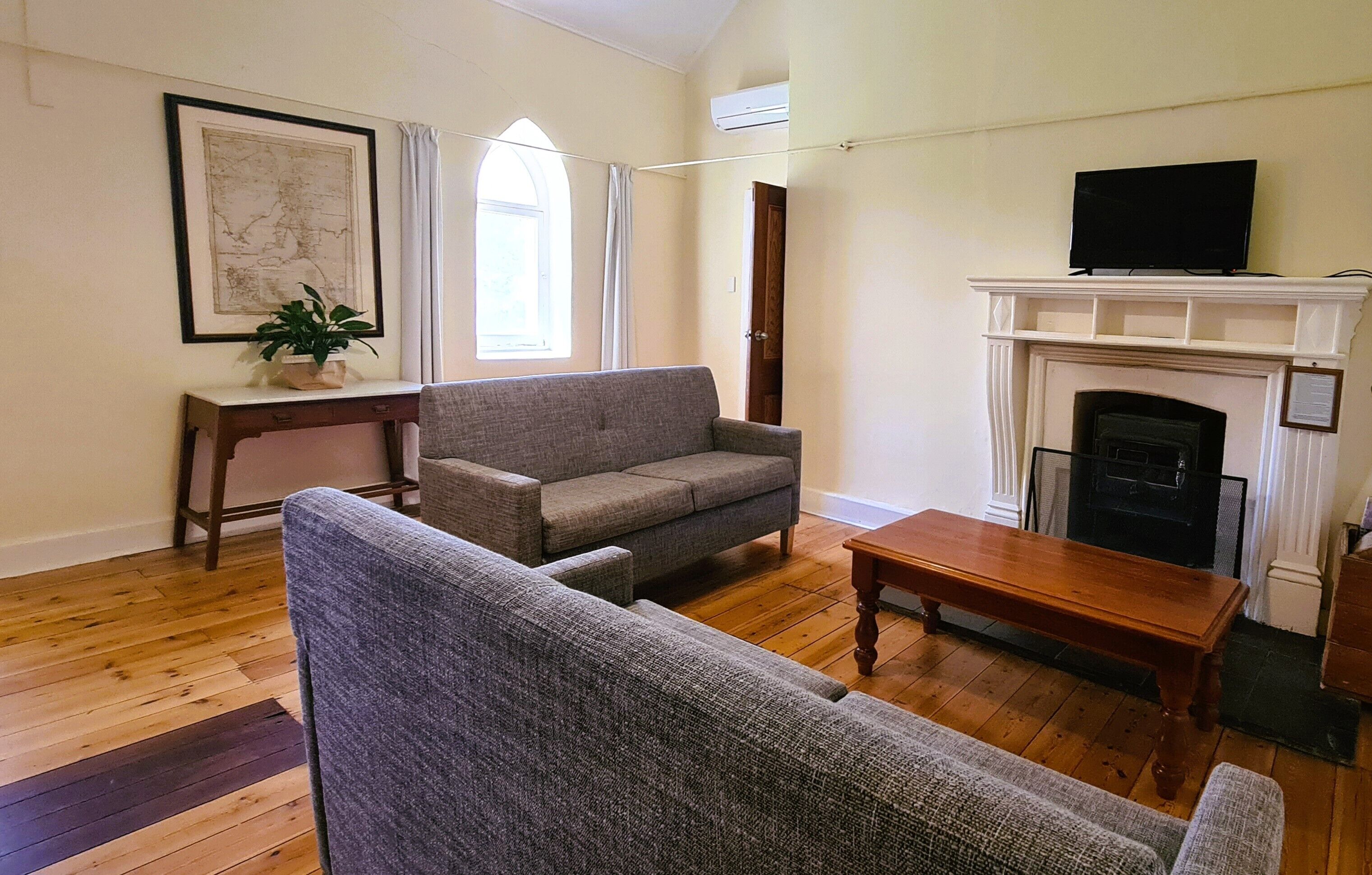 Ein Wohnzimmer mit grauem Sofa, einem Holztisch, einem Kamin und einem Fernseher auf einer Konsole.