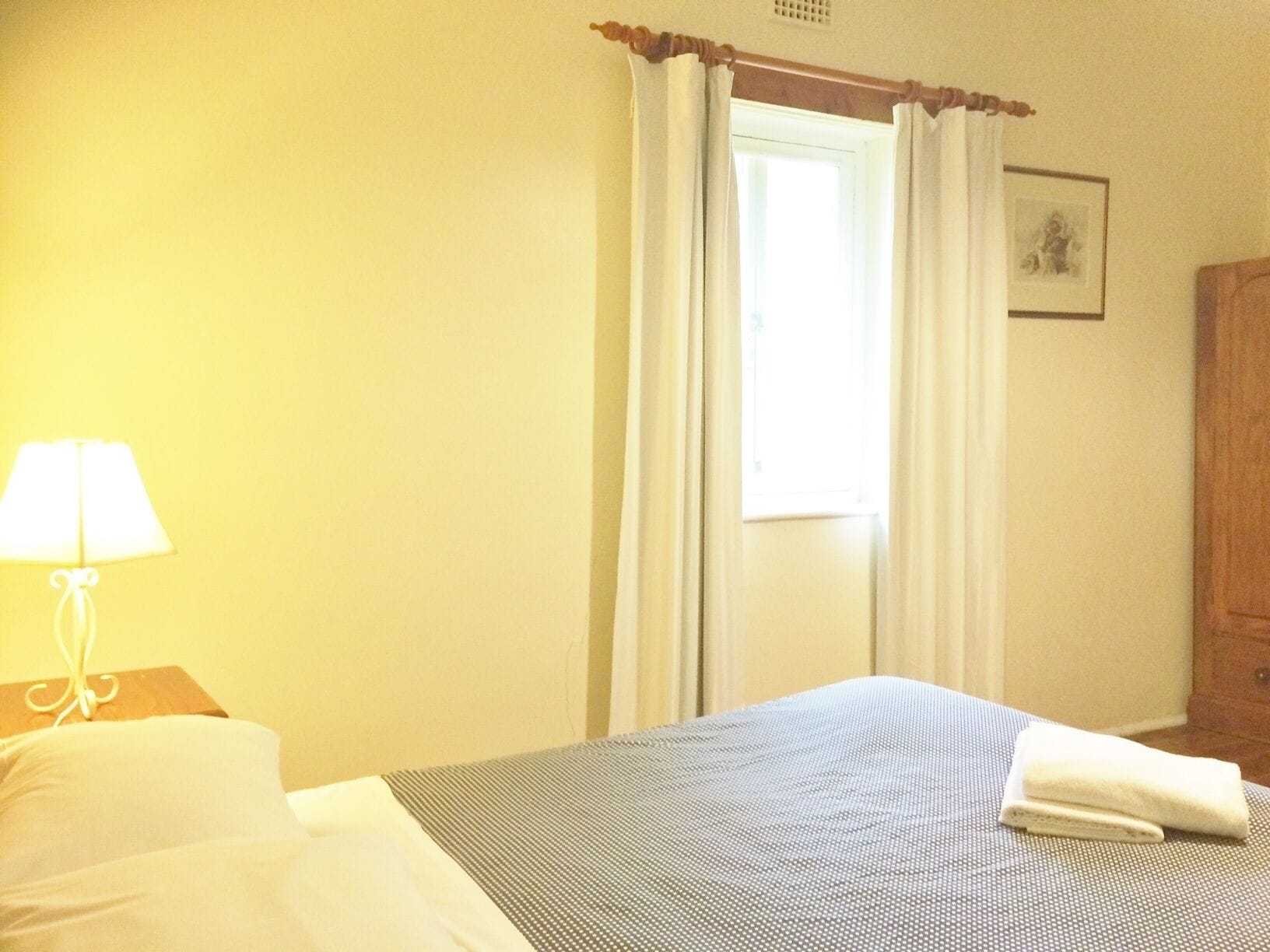 Ein Hotelzimmer mit einem Bett, einem Nachttisch mit Lampe, einem Fenster mit Vorhängen und einem Holzschrank.