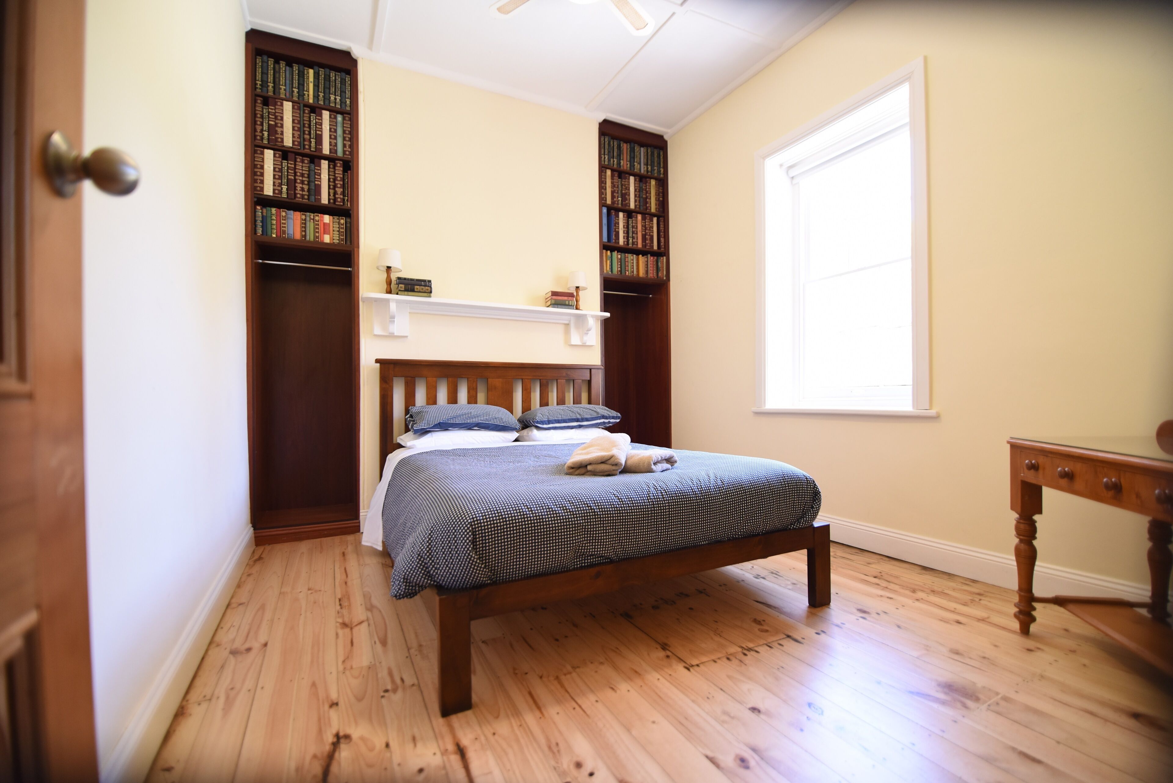 A bedroom with a wooden bed, a nightstand, a bookshelf, and a window.