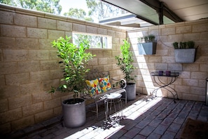 A patio area with a metal bench, two potted plants, and a metal table.