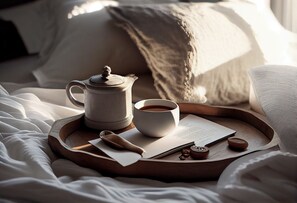A wooden tray with a teapot, cup, spoon, and a menu on a bed with white linens.