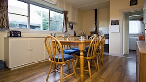 Een compacte keuken met een eethoek, met een ronde houten tafel, blauwe stoelen met kussens, en een ingebouwde kookplaat.