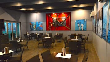 Een restaurant met tafels en stoelen, ruim opgezet, met kunstwerken aan de muur en een modern plafondontwerp.