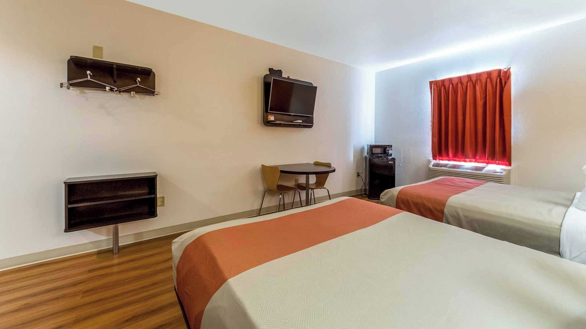 A hotel room with two beds, a TV, a desk with a chair, a coffee machine, and a window with curtains.