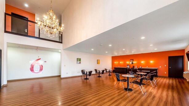 A spacious room with a wooden floor, a chandelier, and a reception desk. - Motel 6 Jourdanton, TX (Jourdanton)