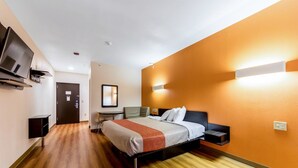 A hotel room with a bed, bedside tables, a TV, and a mirror. - Motel 6 Jourdanton, TX (Jourdanton)