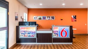 A reception desk with a large '6' sign, a computer station, and framed pictures on the wall. - Motel 6 Jourdanton, TX (Jourdanton)