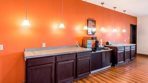 A hotel reception area with a wooden floor, a counter with a coffee machine, and a sign indicating morning charge for no charge. - Motel 6 Jourdanton, TX (Jourdanton)