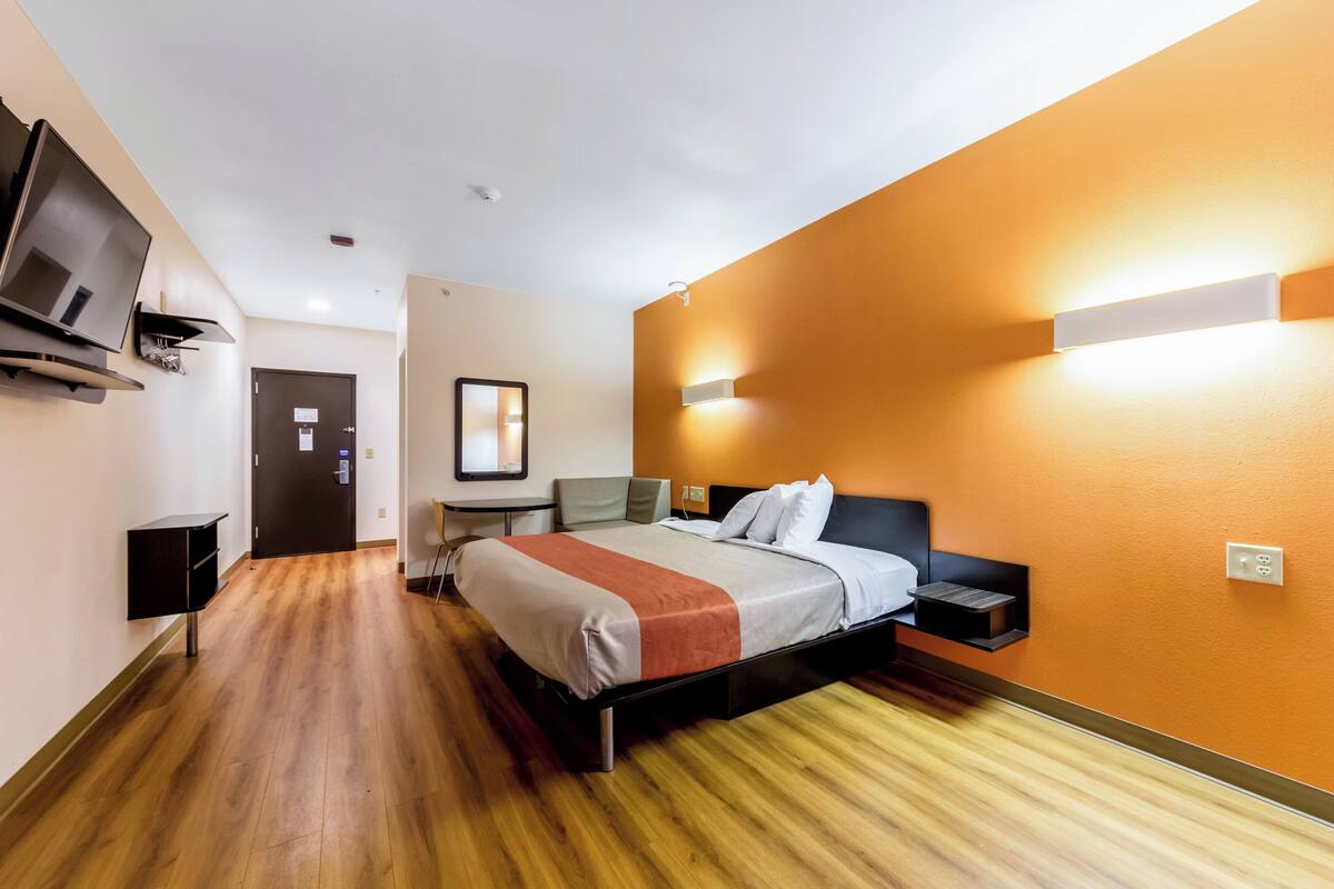 A hotel room with a bed, a TV, a desk, and a wall-mounted light.