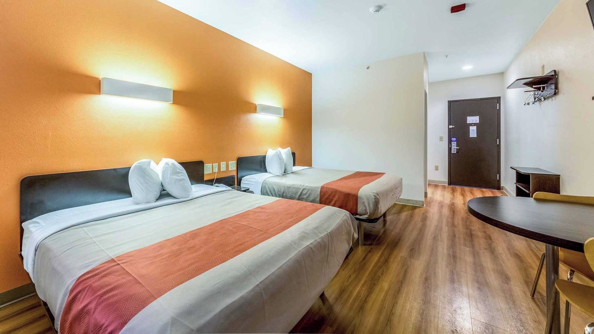 A hotel room with two beds, a desk, and a chair.