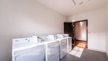 A laundry room with four Whirlpool dryers, a dark wooden floor, and a white ceiling with recessed lighting.