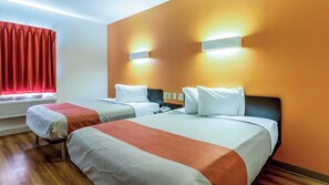 Quarto de hotel com duas camas, janela com cortinas vermelhas, unidade de ar condicionado e luminárias fixadas na parede.