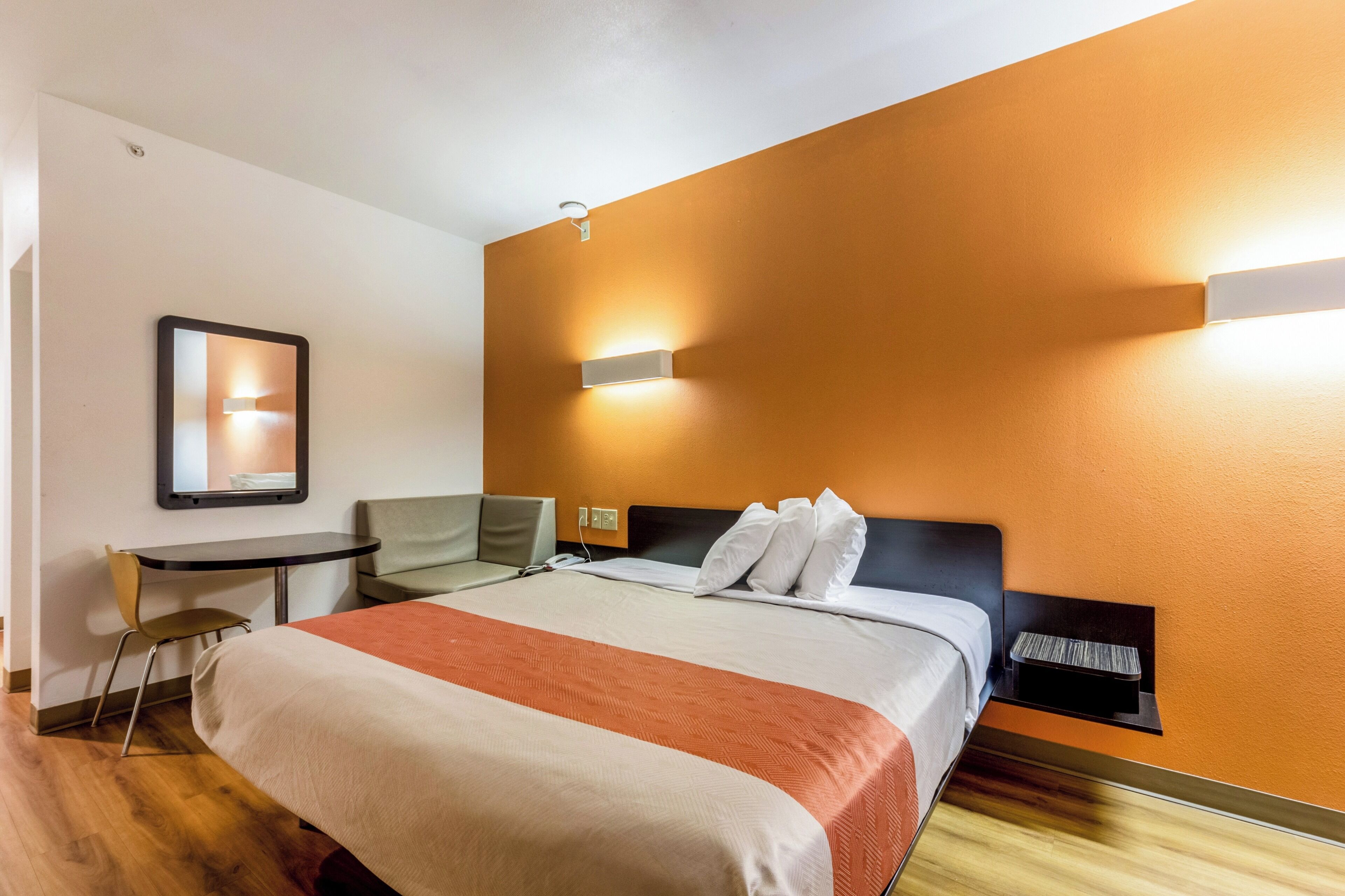 Una habitación de hotel con una cama, un escritorio, una silla y una lámpara fijada a la pared.