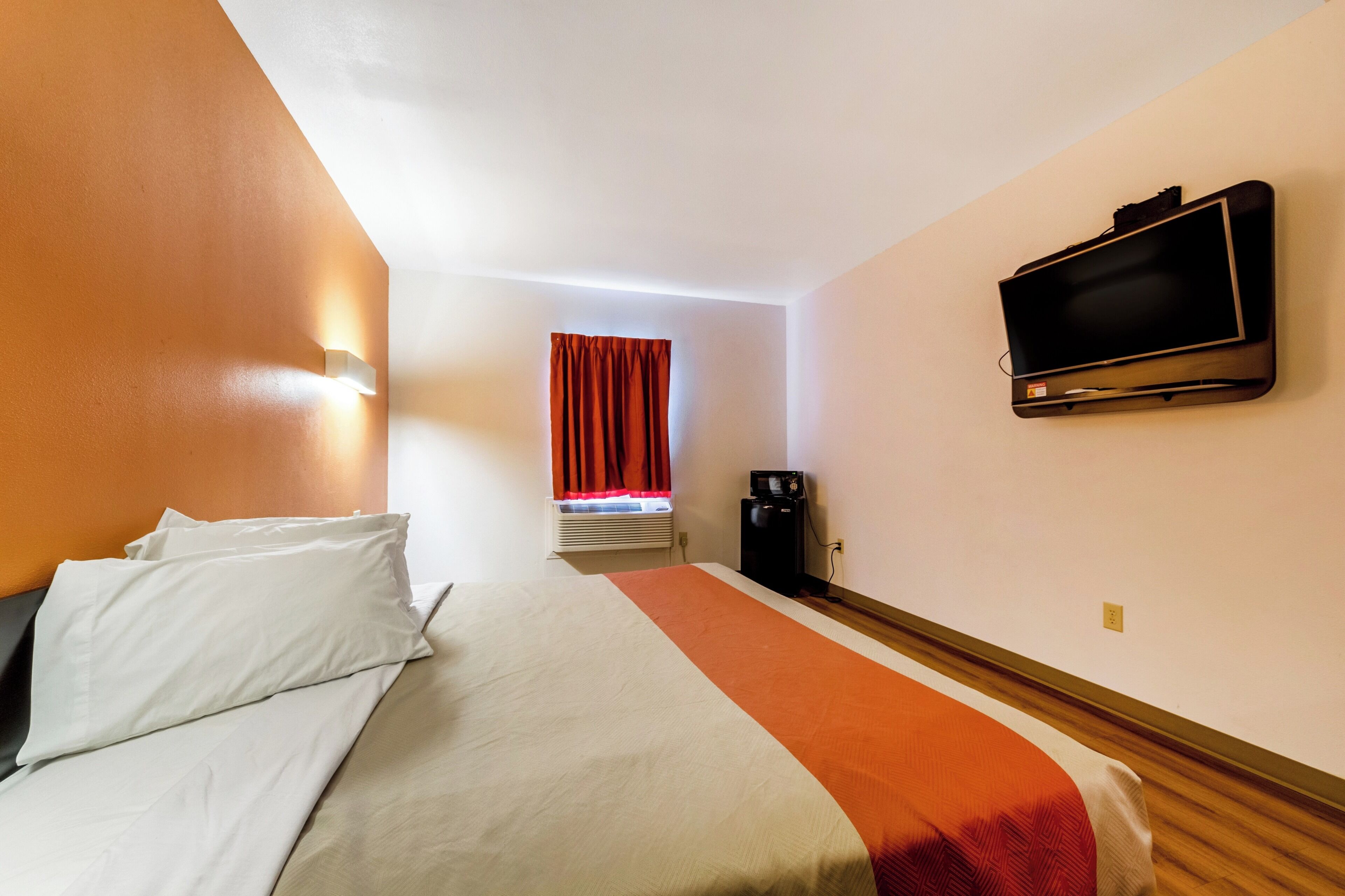 Una habitación de hotel con cama, televisión, ventana con cortinas y cafetera.
