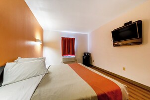 Una habitación de hotel con cama, televisión, ventana con cortinas y cafetera.