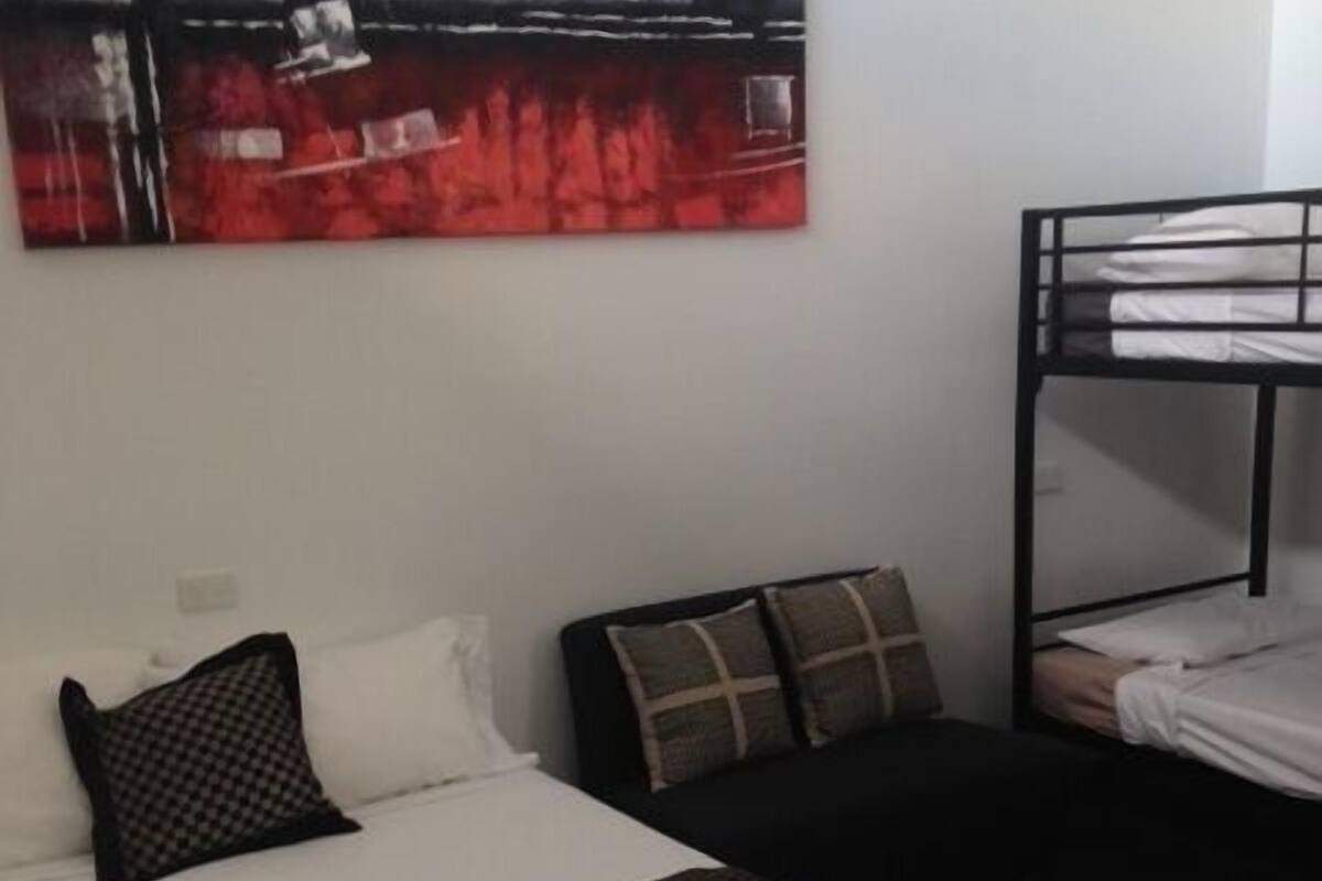 A hotel room with a bunk bed, a single bed with a patterned bedspread, and a large abstract painting on the wall.