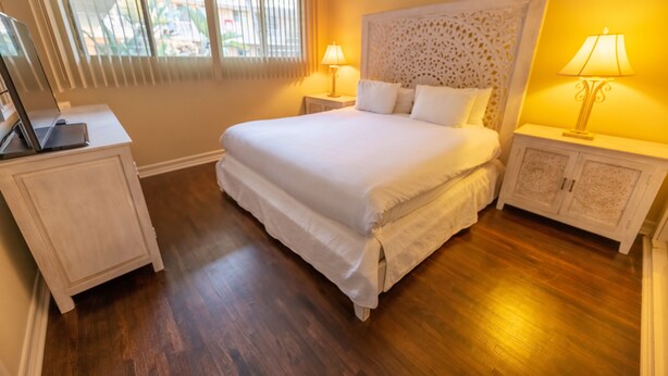 A neatly arranged bedroom with a large bed, two bedside tables, and a window with blinds. - Cal Mar Hotel Suites (Santa Monica)