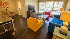 A living room with a sofa, a television, and a dining area with chairs and a table. - Cal Mar Hotel Suites (Santa Monica)