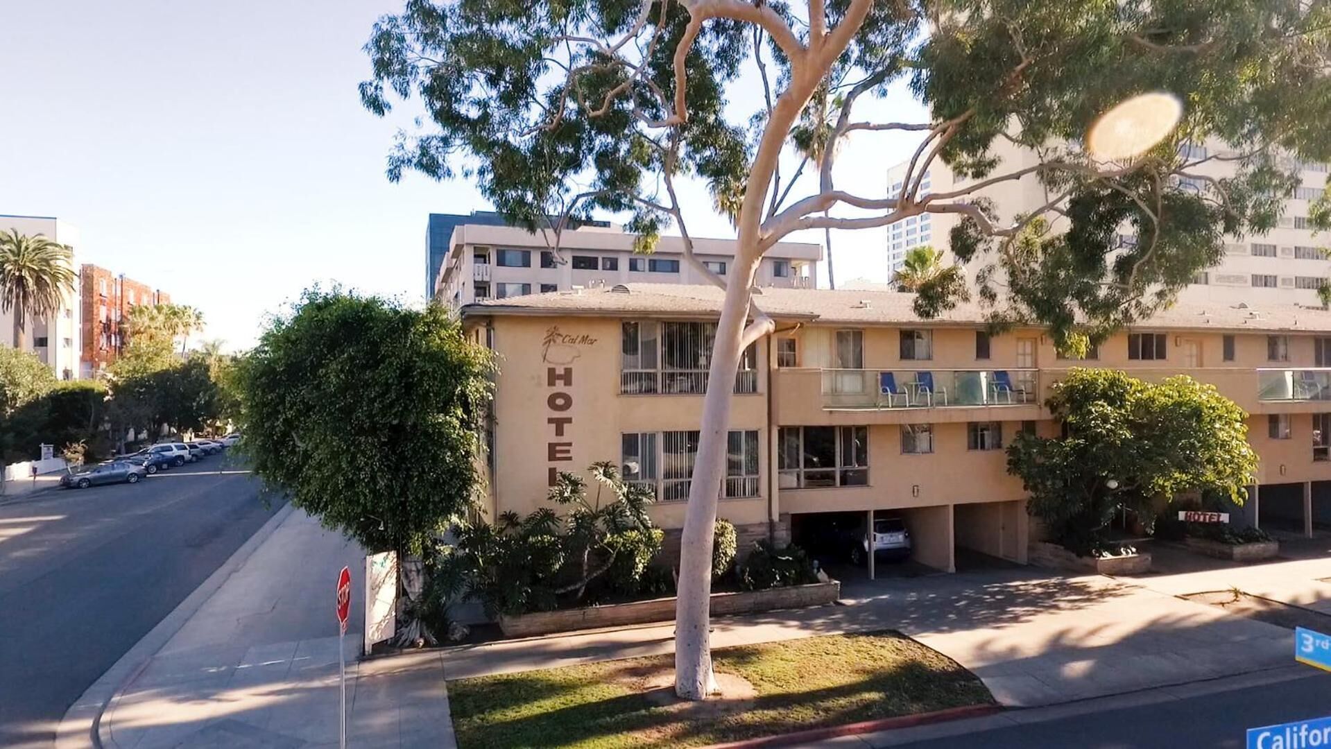 Um hotel com uma placa 'HOTEL' na fachada, vários andares e uma área de estacionamento visível.
