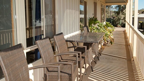 A covered outdoor patio with wicker chairs and a table, large windows, and a view of the surrounding landscape. - Black Jack Get-A-Way (Orroroo)
