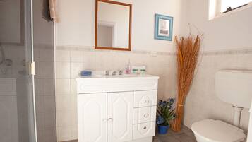 A bathroom with a white vanity, a mirror, a framed picture, a toilet, and a shower area.