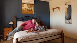 A bedroom with a bed, a nightstand with a lamp, a painting on the wall, and a mirror. - Black Jack Get-A-Way (Orroroo)