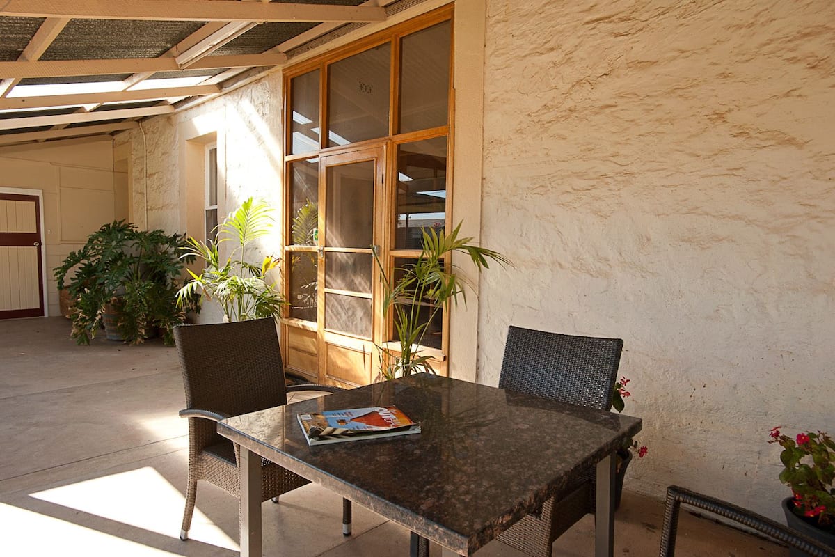 An outdoor patio with a glass table, wicker chairs, and potted plants.