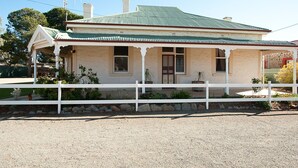 A two-story house with a green metal roof, a white porch, and a white fence. - Black Jack Get-A-Way (Orroroo)