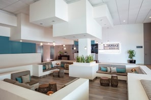 Una hall d'albergo moderna con diverse aree salotto, una reception e un cartello con la scritta 'Gamma de Fiesta inn'.