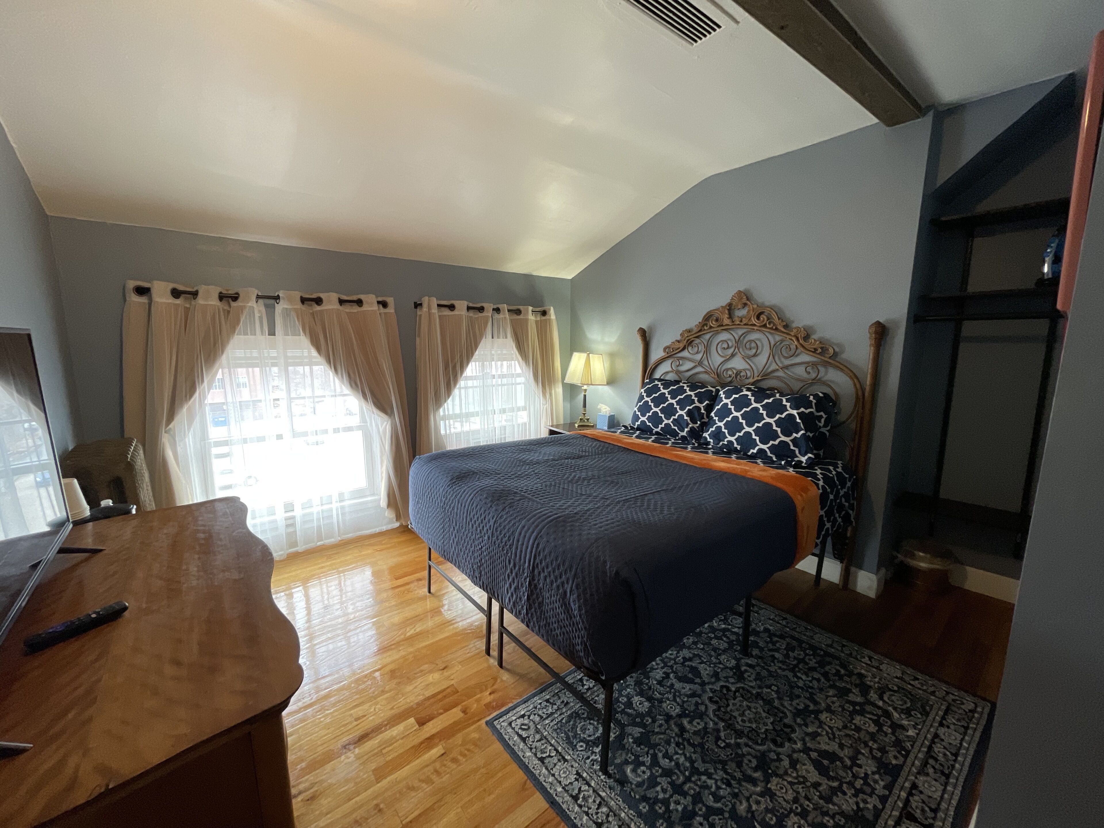 A bedroom with a bed, wooden desk, and a nightstand with a lamp.