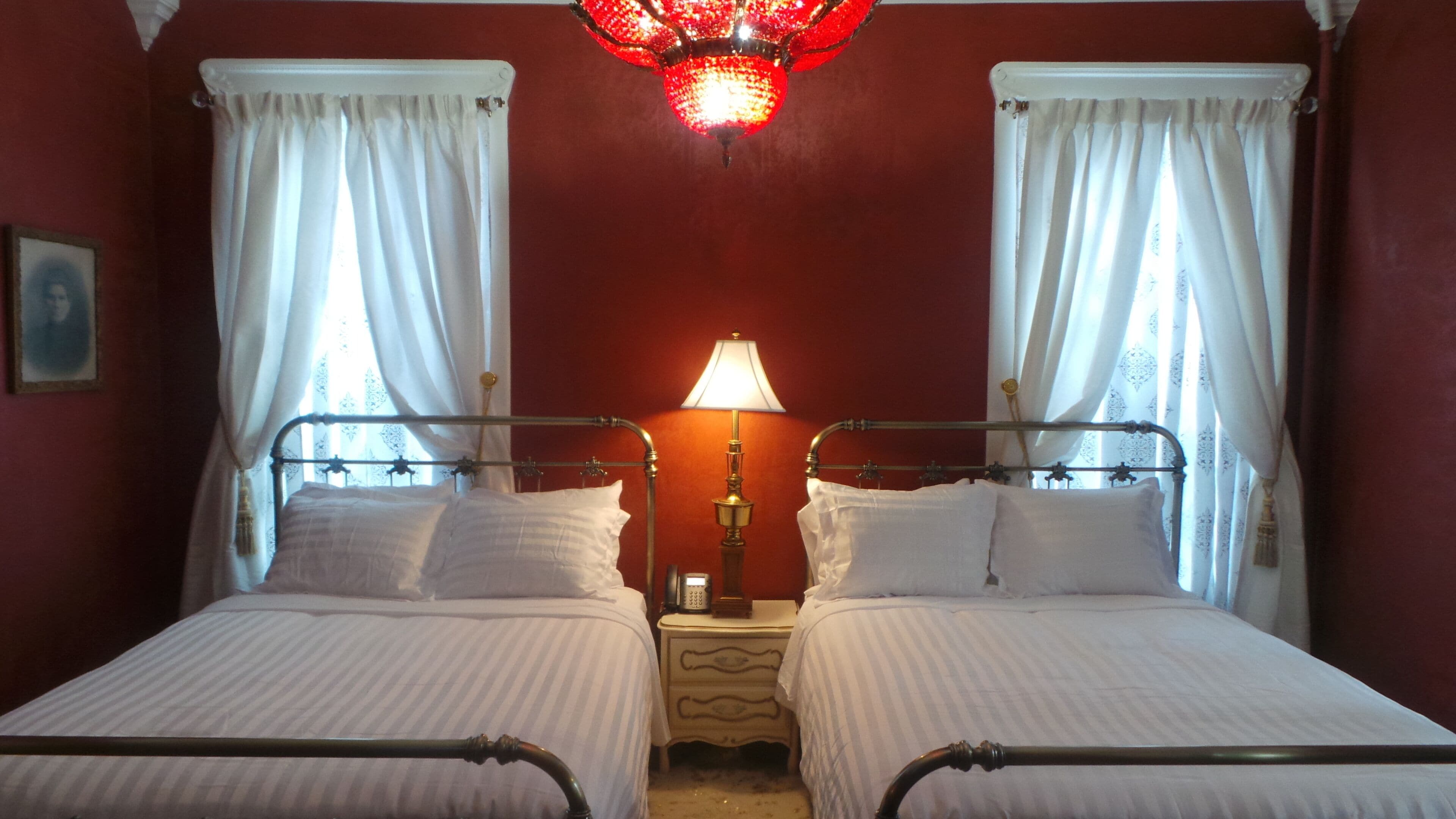 Una habitación con dos camas, ropa de cama blanca, una mesita de noche con lámpara y una pared roja.
