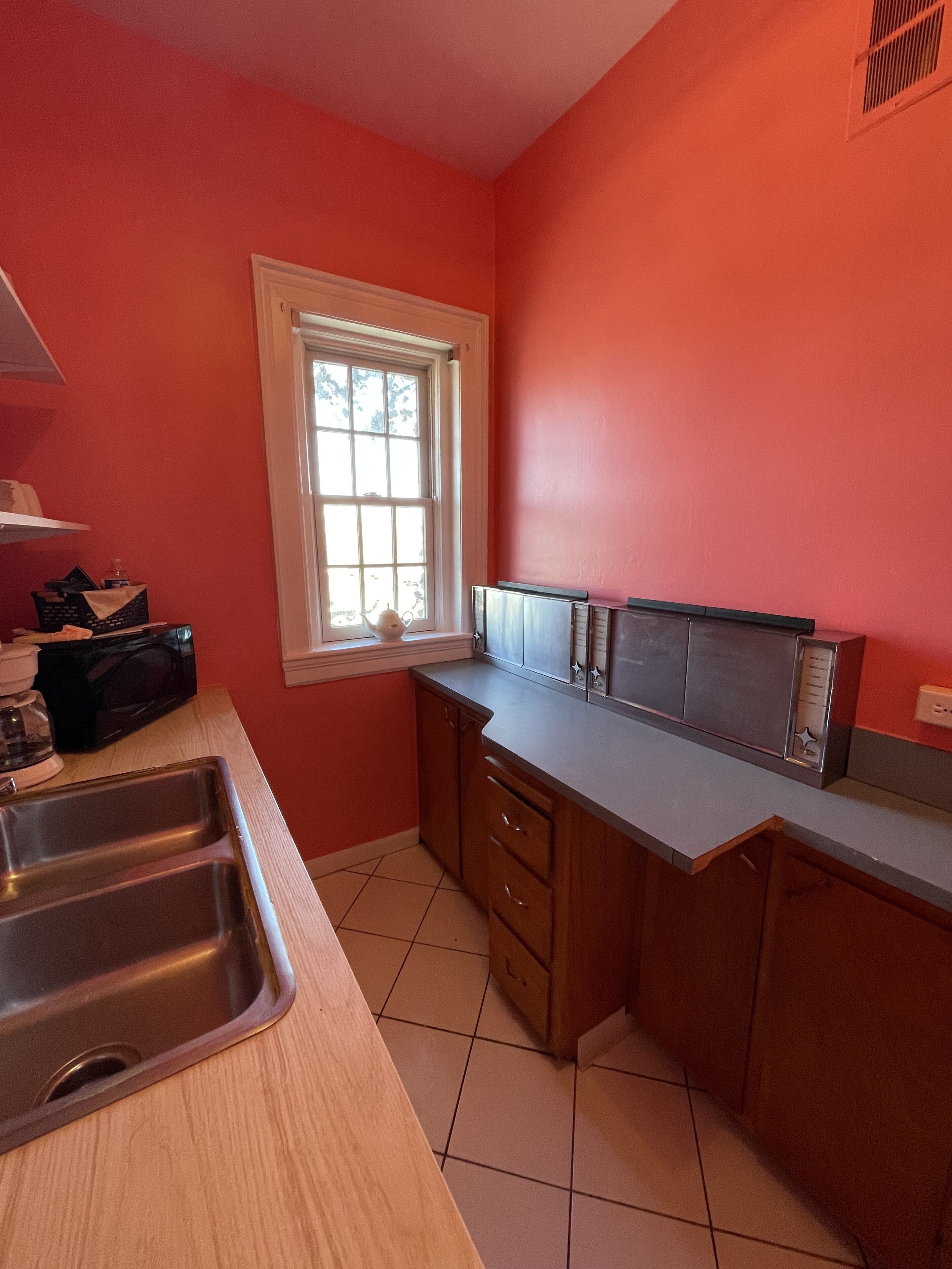 A kitchen with a sink, countertop, cabinets, and a window.