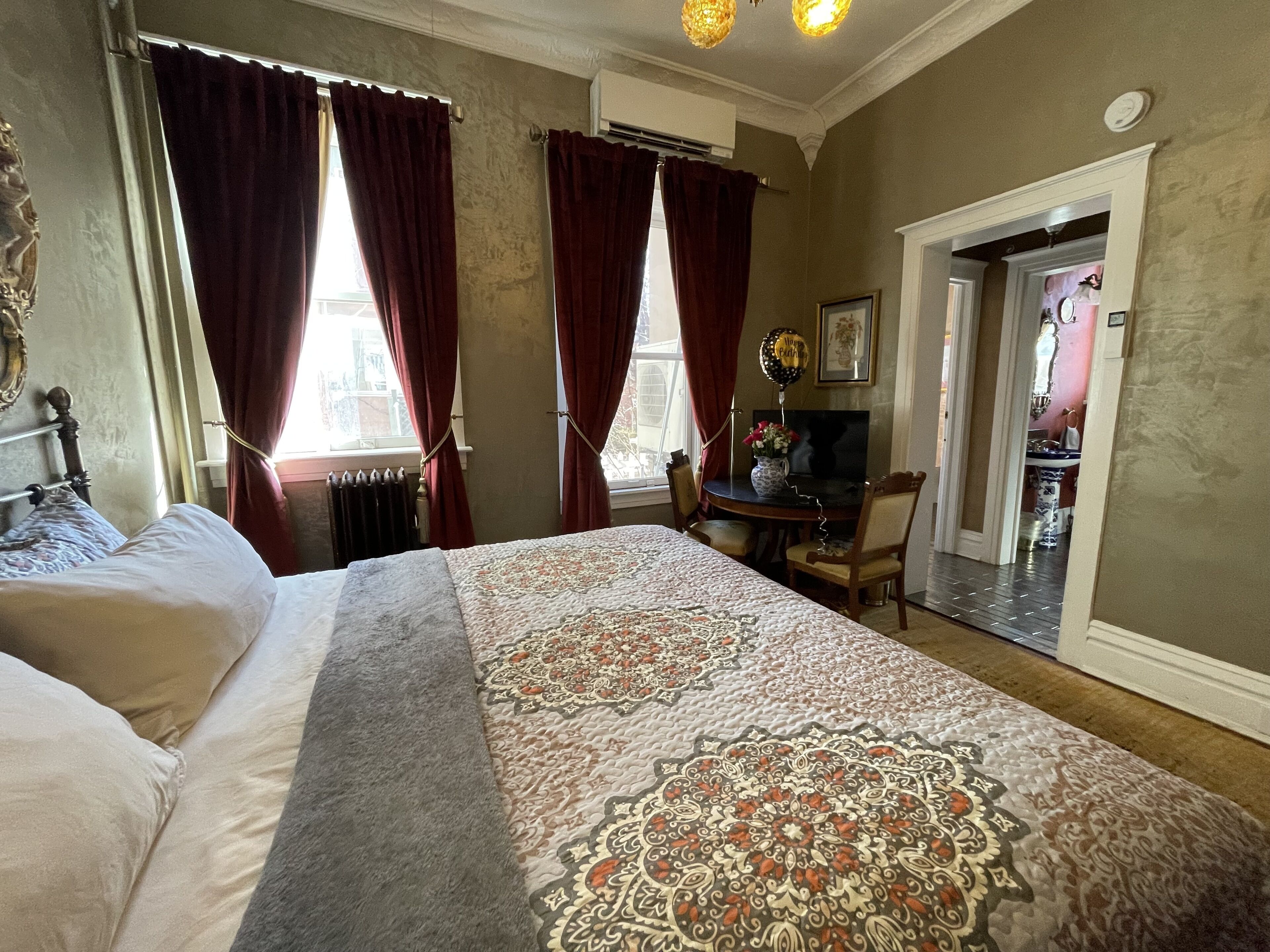 A hotel room with a large bed, a desk with a chair, a radiator, and a door leading to a bathroom.