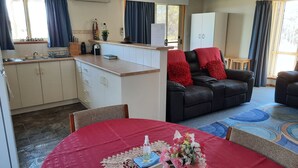 Un espacio habitable compacto con kitchenette, una zona de comedor con mantel rojo, un sofá de cuero negro con cojines rojos y una alfombra estampada.