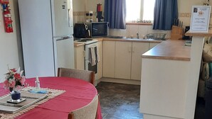 Cocina compacta con refrigerador, microondas y estufa. Una mesa de comedor con sillas está instalada en el centro.
