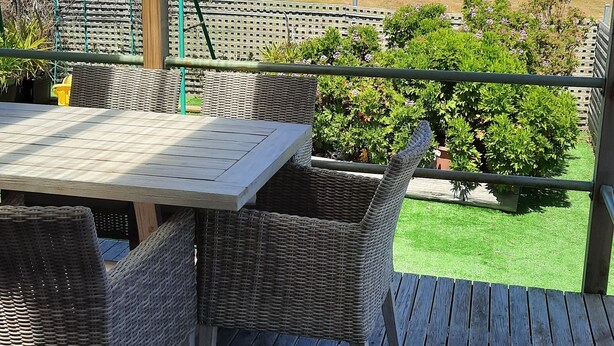 Un espacio al aire libre cubierto con mesa y sillas de mimbre, con vista a un jardín ajardinado y una vista panorámica del mar.