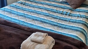 Una cama bien hecha con una colcha a rayas, dos almohadas marrones y una toalla doblada sobre la cama.