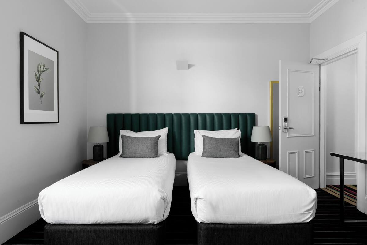 A hotel room with two single beds, a green headboard, a framed picture on the wall, and a door with a sign.